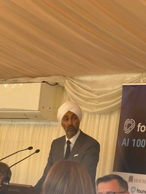 Lord Kulveer Ranger at a lectern in a marquee, next to a Foundever AI 100 banner