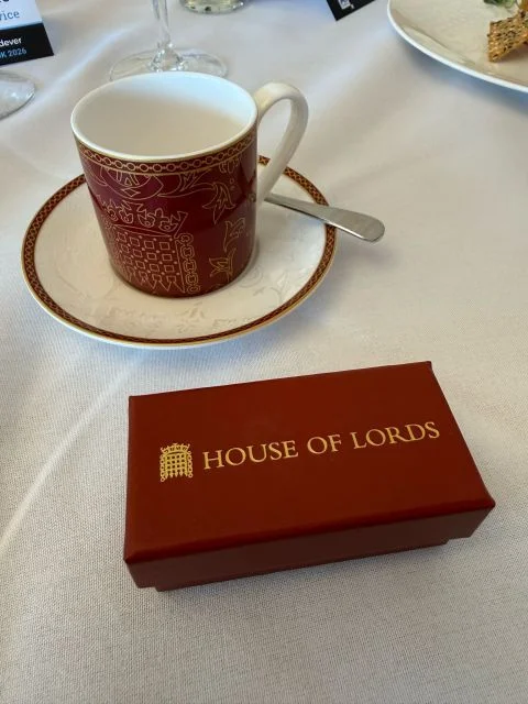 A House of Lords gift box beside a red and gold patterned cup and saucer on a white tablecloth